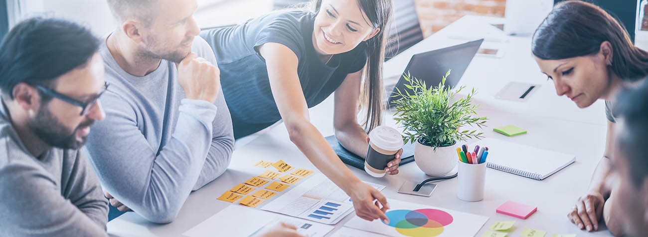 A diverse group of young marketing professionals, male and female, discussing colorful charts and graphs in an office setting