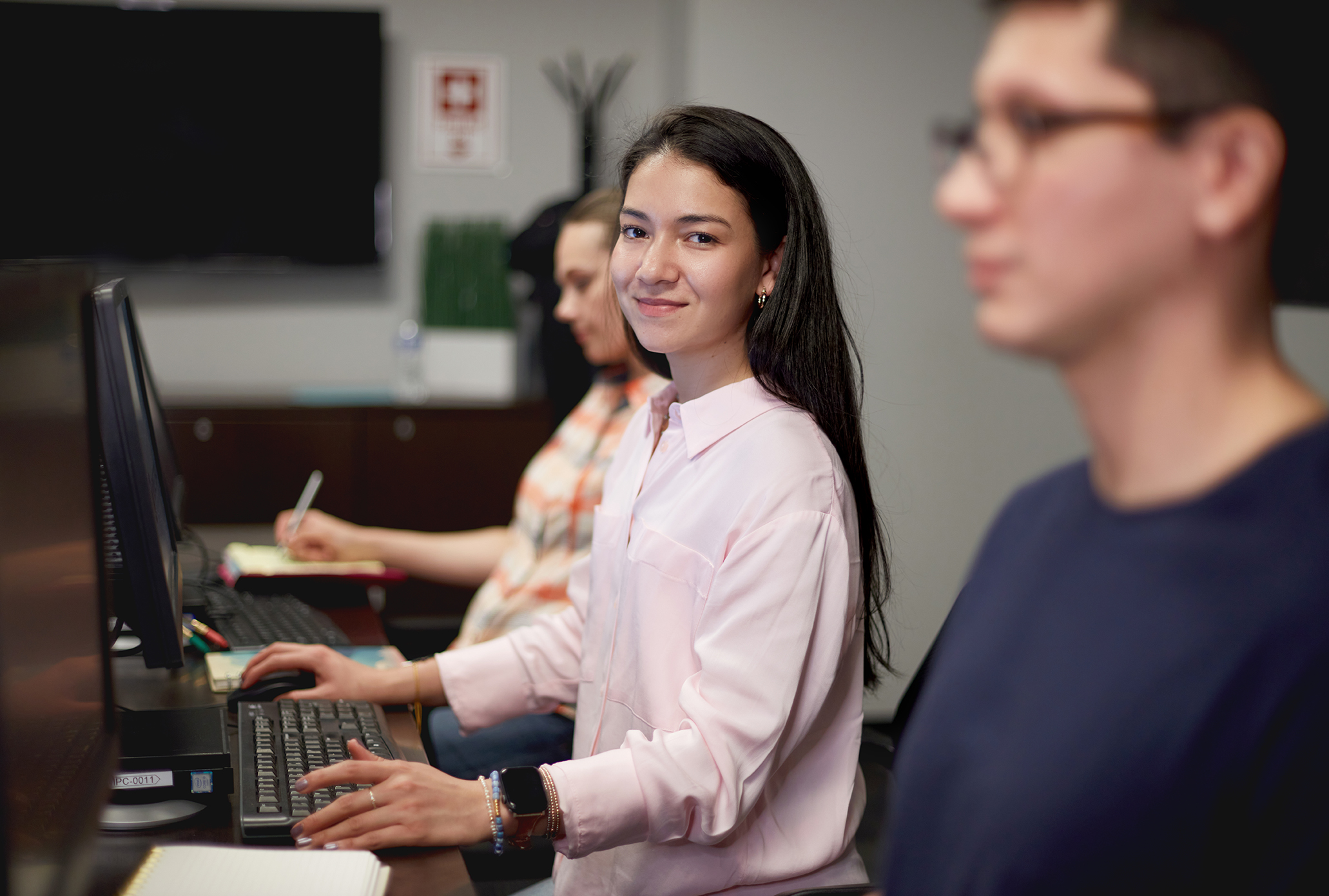 A smiling woman student sitting at a computer in the classroom.