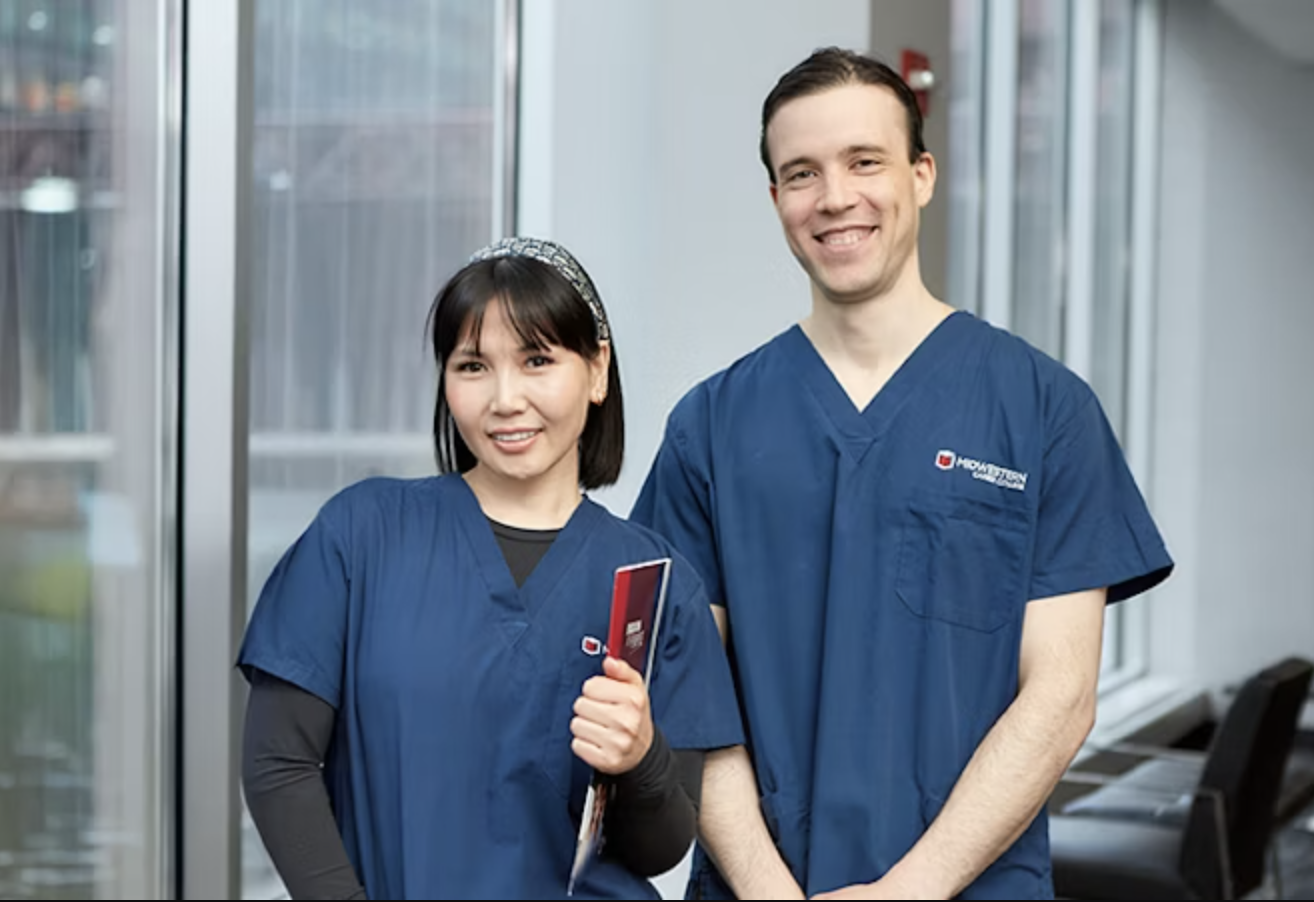 Two MCC ESL students in medical scrubs smiling while standing in the campus hallway.